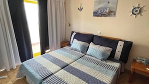 Un letto matrimoniale con biancheria a righe, un comodino, una sveglia a muro e un quadro raffigurante un faro.