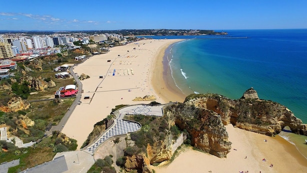 Una spiaggia costiera con una passeggiata lastricata, scogliere rocciose e una vista limpida sull'oceano.