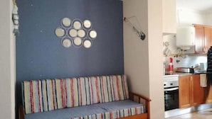 Una stanza con un divano addossato a una parete blu, un angolo cottura con mobili in legno e un lampadario fissato al muro.