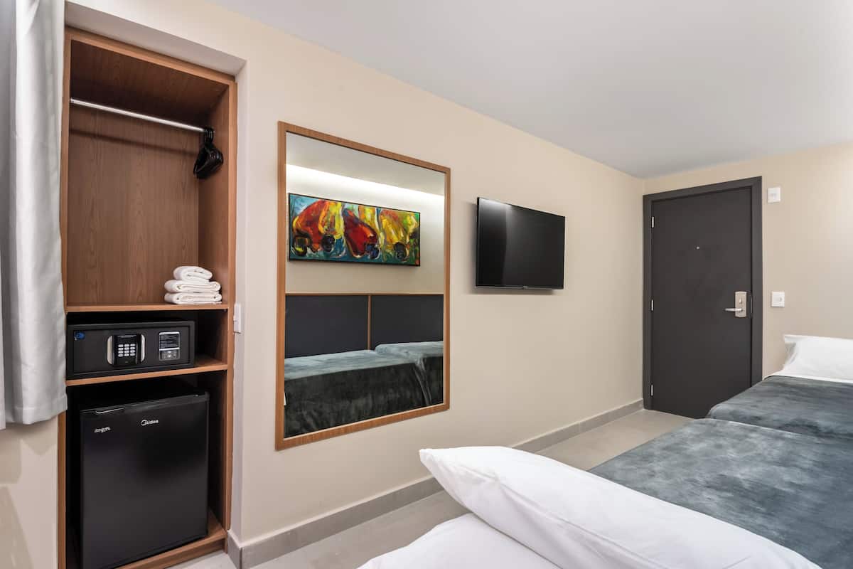 A hotel room with a bed, a wardrobe, a small refrigerator, a microwave, a flat-screen TV, and a painting on the wall.