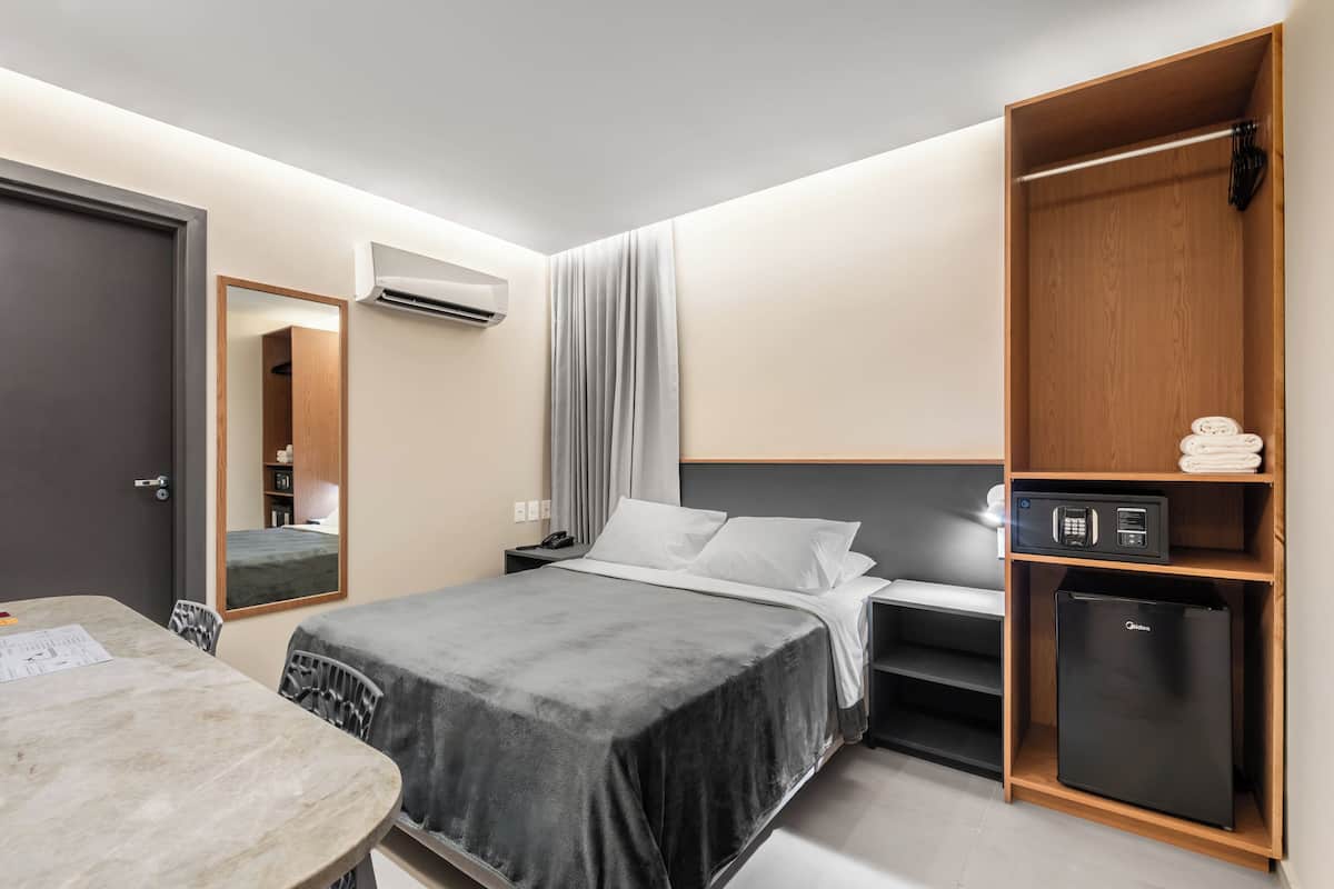 A modern hotel room with a bed, a desk, a wardrobe, and a compact refrigerator.
