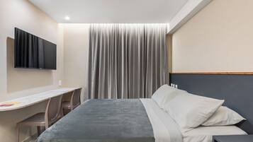 Habitación de hotel con cama, escritorio, silla, televisor montado en la pared y cortina.