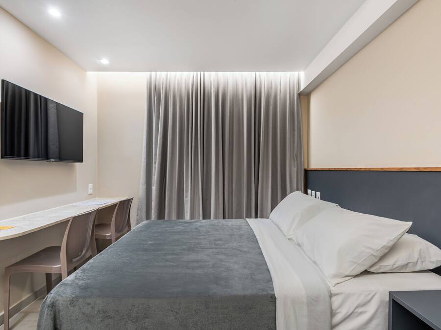 Habitación de hotel con cama, escritorio, silla, televisor montado en la pared y cortina.