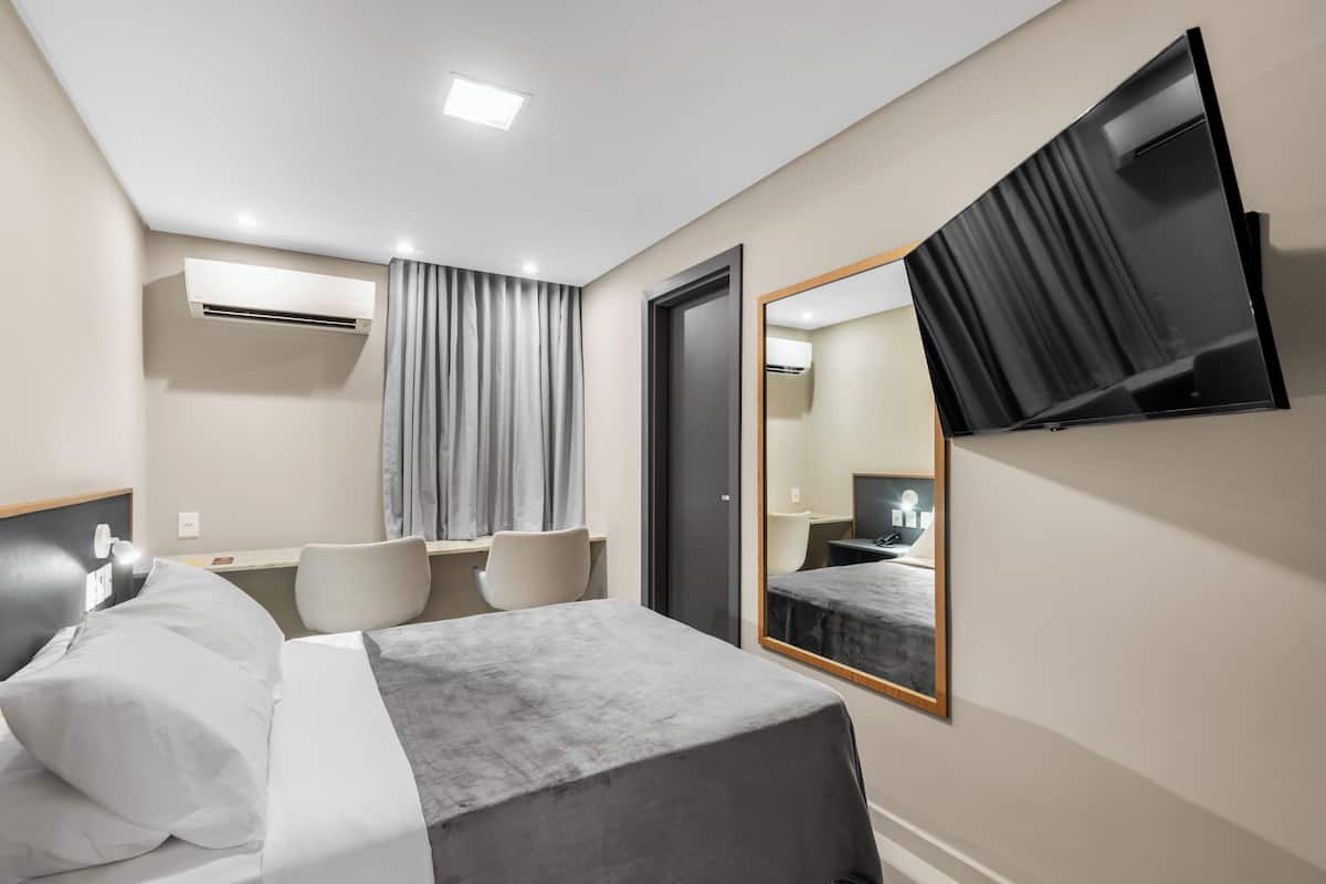 A modern hotel room with a bed, bedside table, chair, and a large mirror.