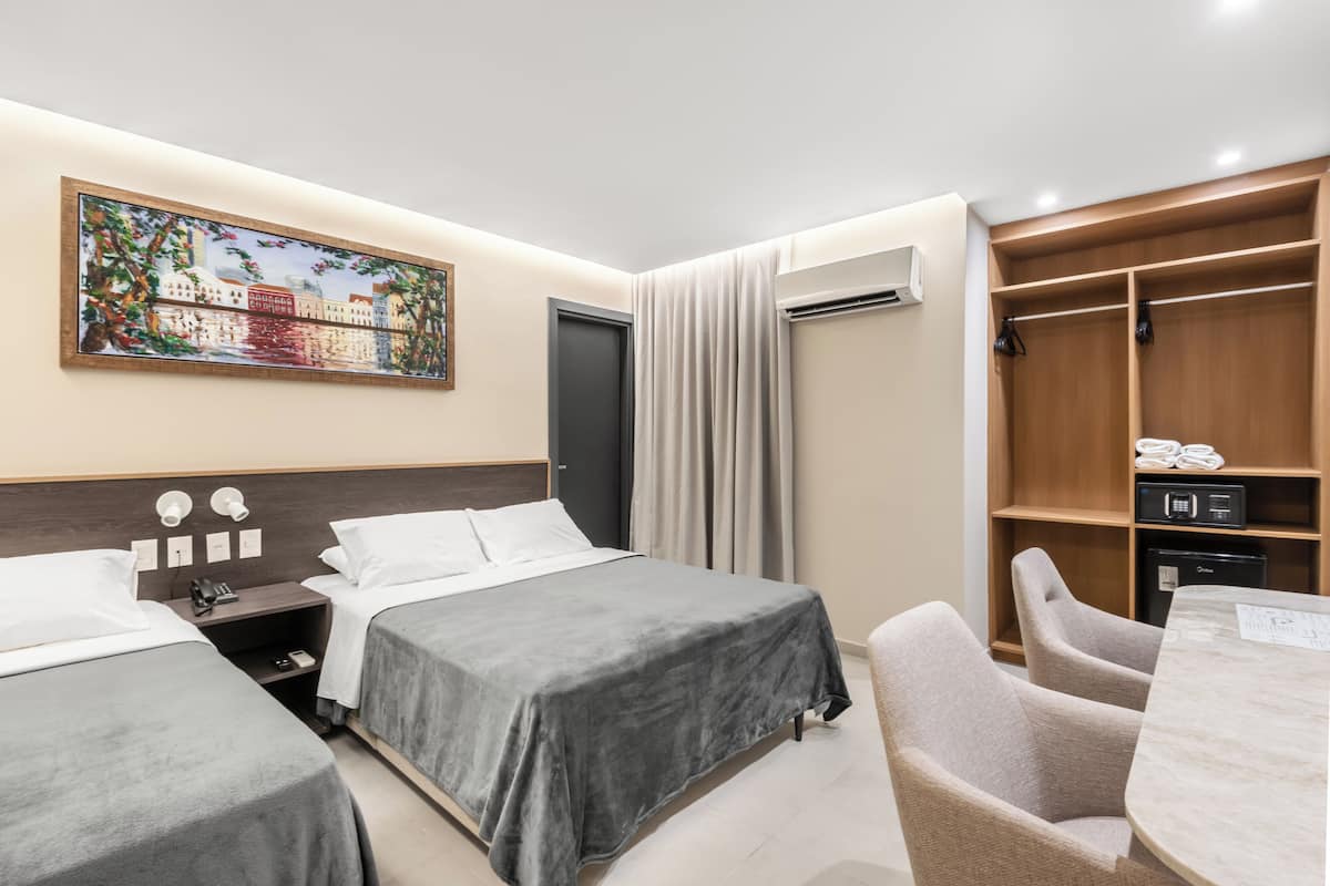 A hotel room with two beds, a desk with a chair, a wardrobe, and a painting on the wall.