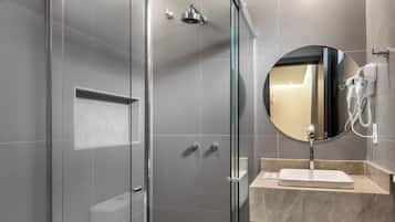 A modern bathroom with a glass-enclosed shower, a round mirror, and a marble sink.