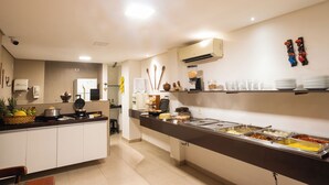 Zona de buffet con diferentes estaciones de comida, un refrigerador y una máquina de café.