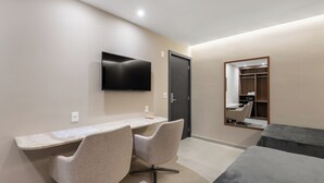 Una habitación de hotel moderna con escritorio, dos sillas, televisor de pantalla plana, armario y cama.