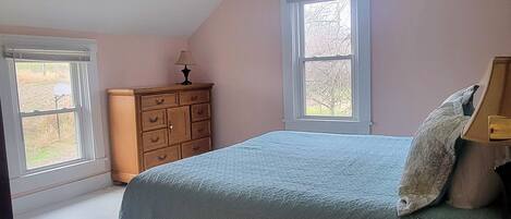 Un dormitorio con cama, cómoda y dos ventanas.