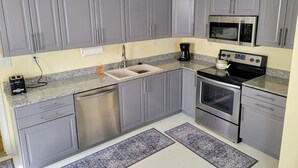 Una cocina compacta con armarios grises, un lavavajillas de acero inoxidable, un microondas, un horno y una cafetera.