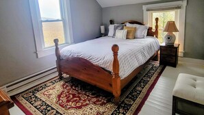 Un dormitorio con cama de madera, alfombra estampada, una mesita de noche y ventana con vistas.