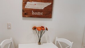 A white dining table with two chairs, a wooden sign with the word "home" above it, and a vase with orange flowers on the table. - Nashville Haven Hideaway- Cozy 3 Bedroom House (Nashville)