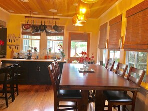 A dining area with a wooden table and chairs, a kitchen with hanging pots, and large windows with blinds. - The Foster Harris House (Washington)