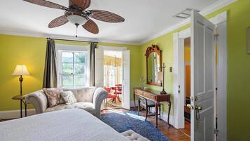 A bedroom with a bed, a desk, a chair, a mirror, and a ceiling fan.