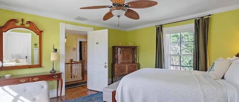 A bedroom with a bed, a ceiling fan, a dresser, a mirror, and a window with curtains.