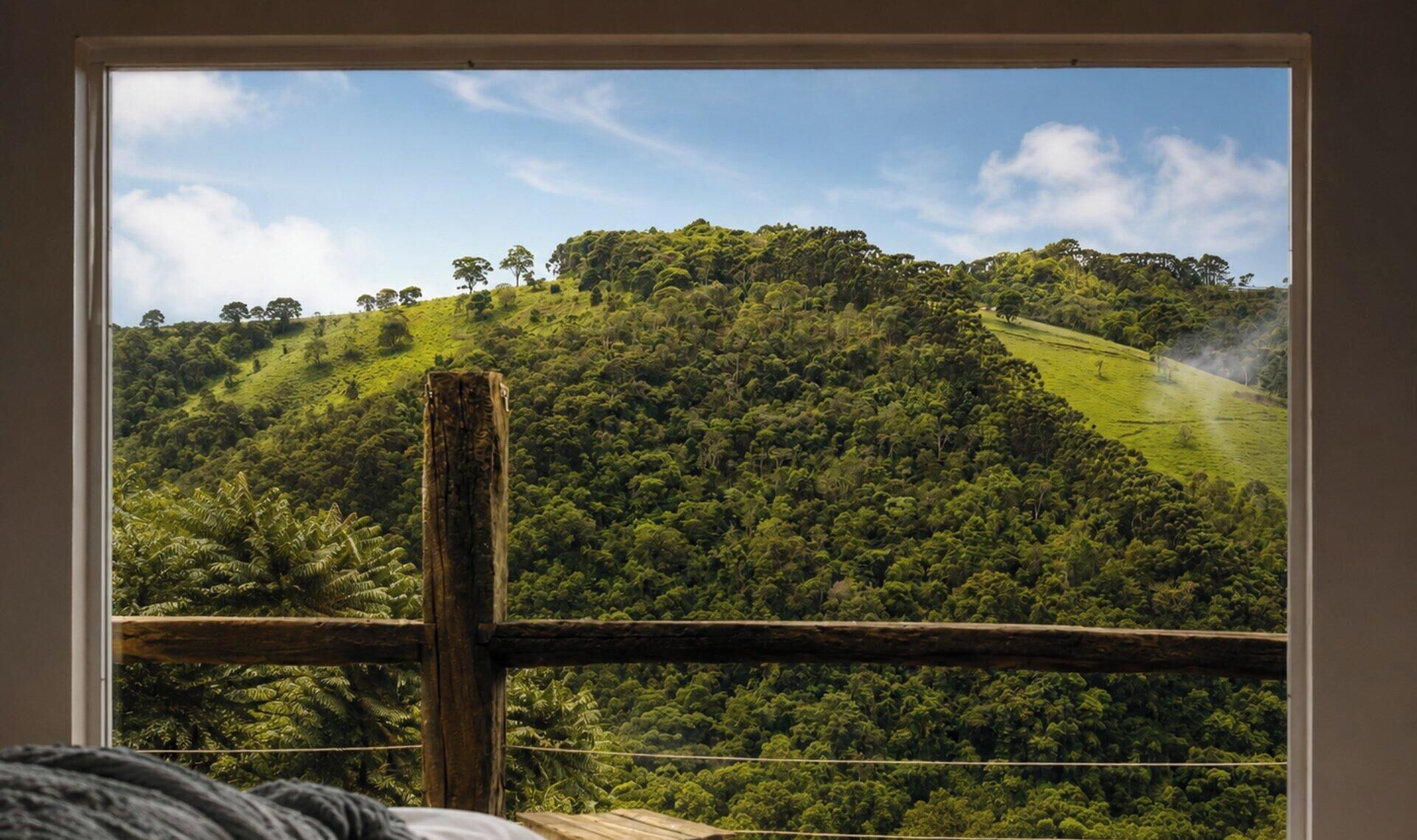 A view through a window of a lush green landscape with a wooden fence in the foreground.