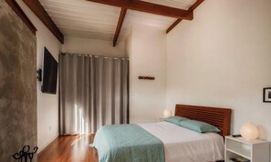 Een slaapkamer met een bed, nachtkastje, een aan de muur bevestigde televisie en een gordijn.