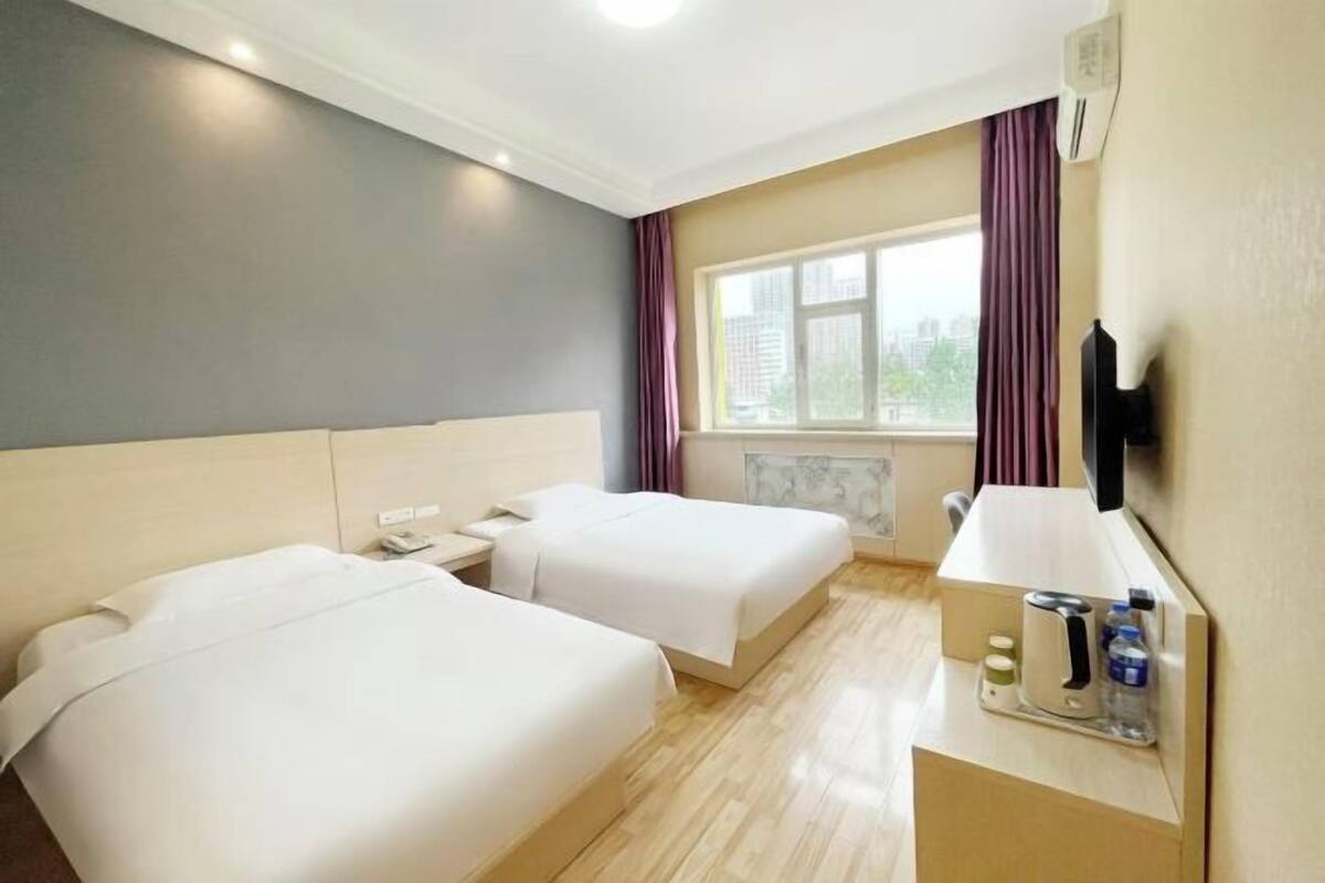 A hotel room with two beds, a desk with a lamp, a TV, and a window with curtains.