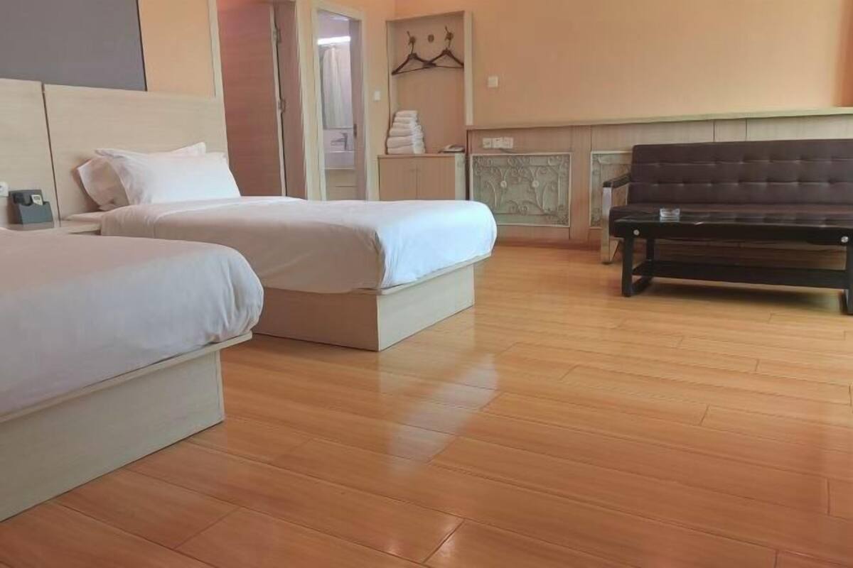A hotel room with two beds, a wooden floor, a bench, and a wardrobe.