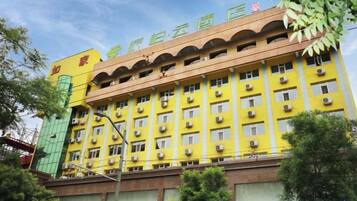 A multi-story building with a yellow facade, multiple windows, and a green entrance.