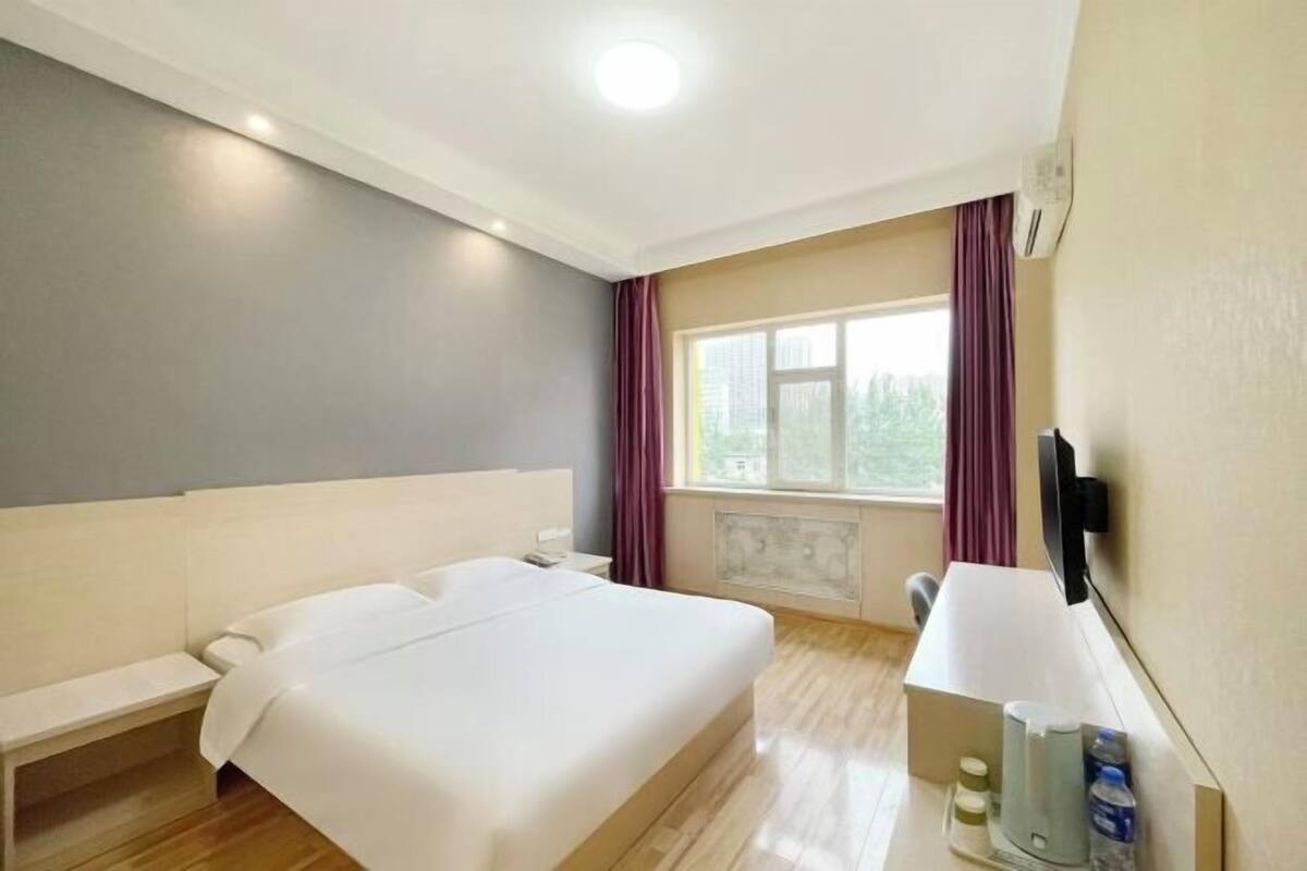 A hotel room with a bed, bedside table, lamp, and window with curtains.
