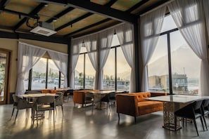 A spacious indoor area with large windows, a table, chairs, and orange seating. - FortuNorth  (Wazirpur)