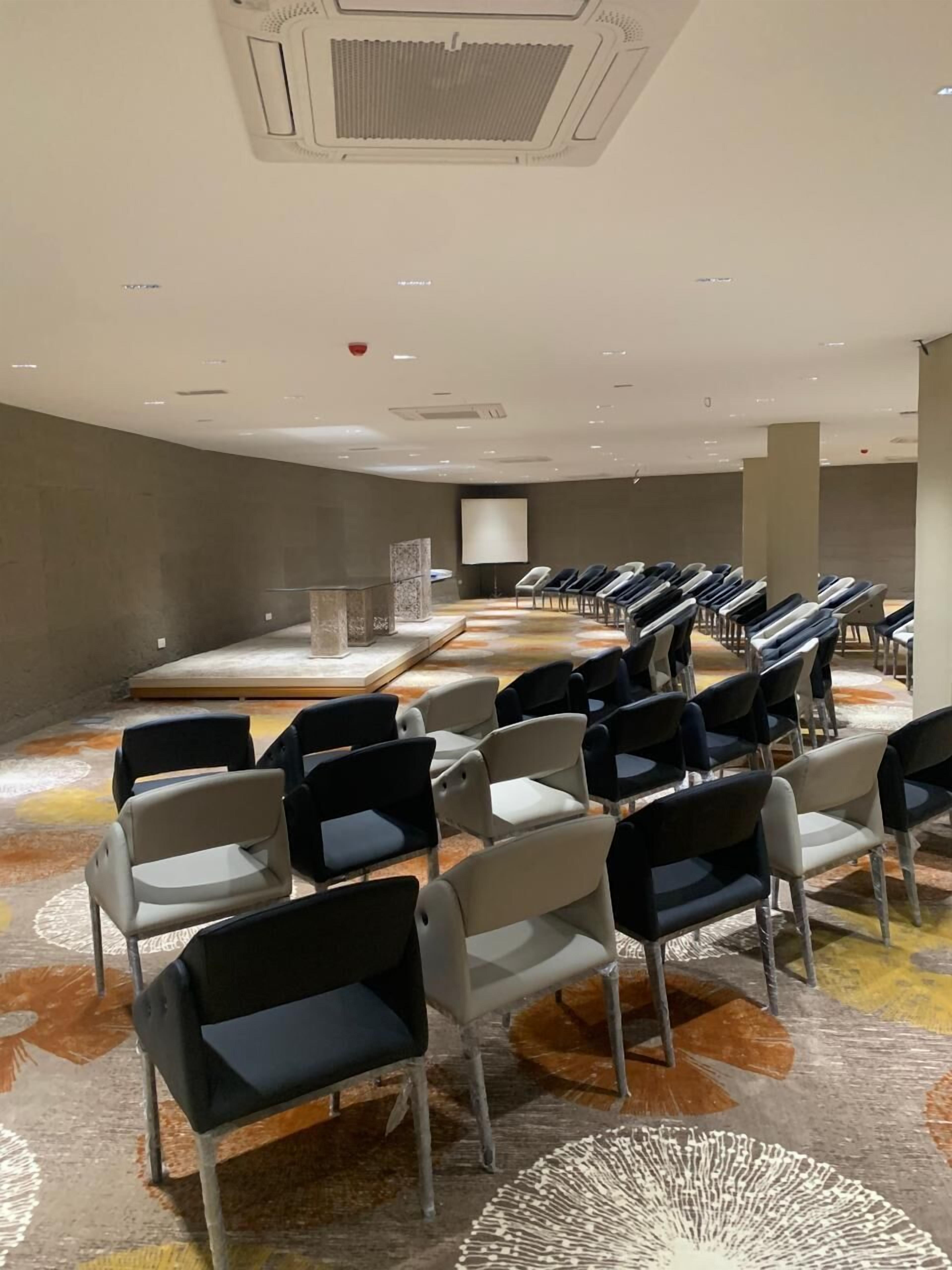Une salle de conférence avec des rangées de chaises, un pupitre et un écran de projection.