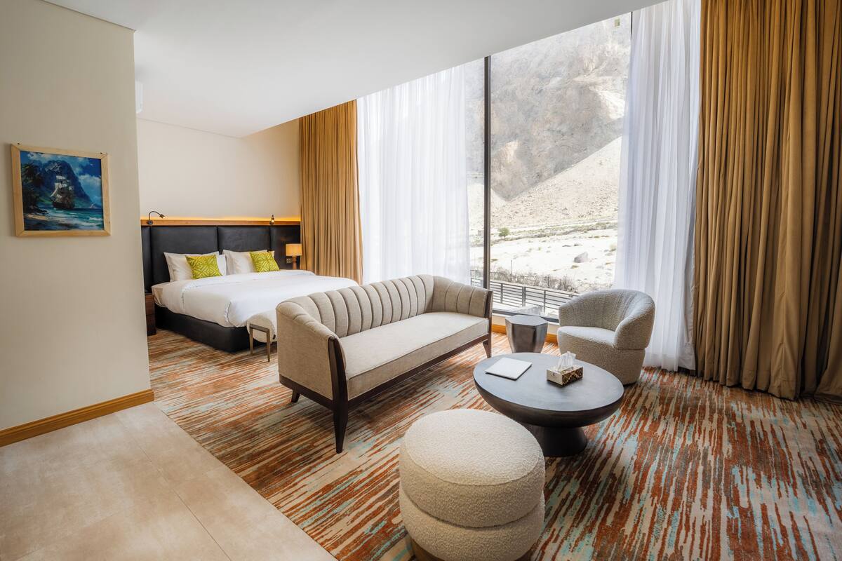 A hotel room with a bed, sofa, armchair, and a small table.