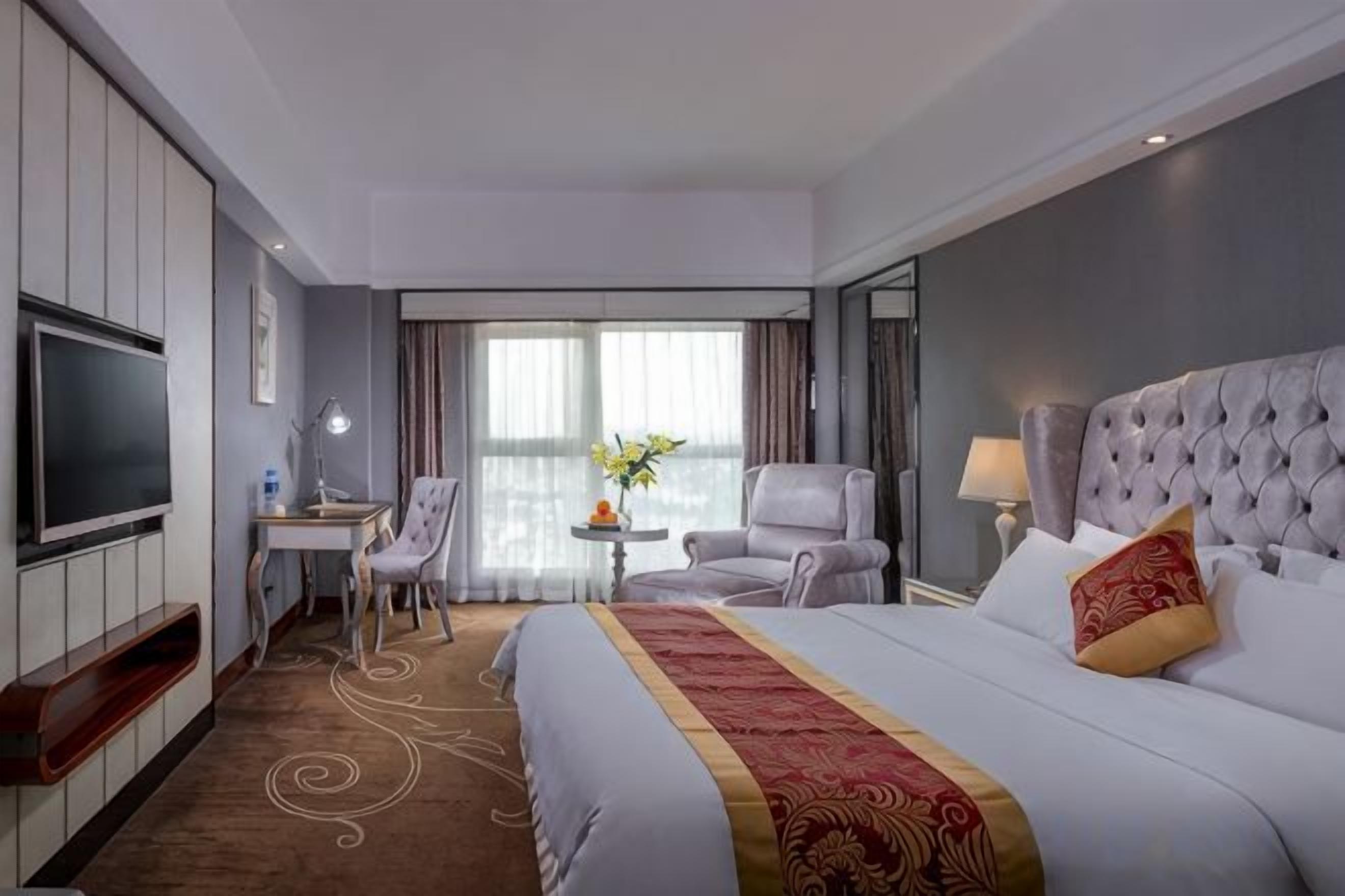 A hotel room with a large bed, a desk, a chair, a TV, and a window with curtains.