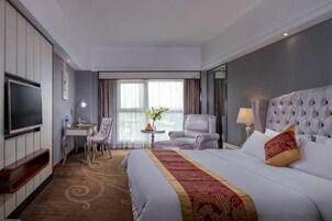 Una habitación de hotel con una cama grande, un escritorio, una silla, un televisor y una ventana con cortinas.