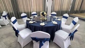 Une table ronde recouverte d’une nappe sombre, entourée de chaises blanches ornées de rubans bleus, préparée pour un événement officiel.