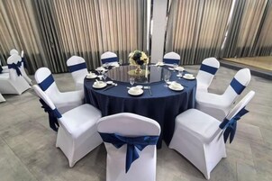 Una mesa redonda con mantel oscuro, rodeada de sillas blancas con cintas azules, preparada para un evento formal.