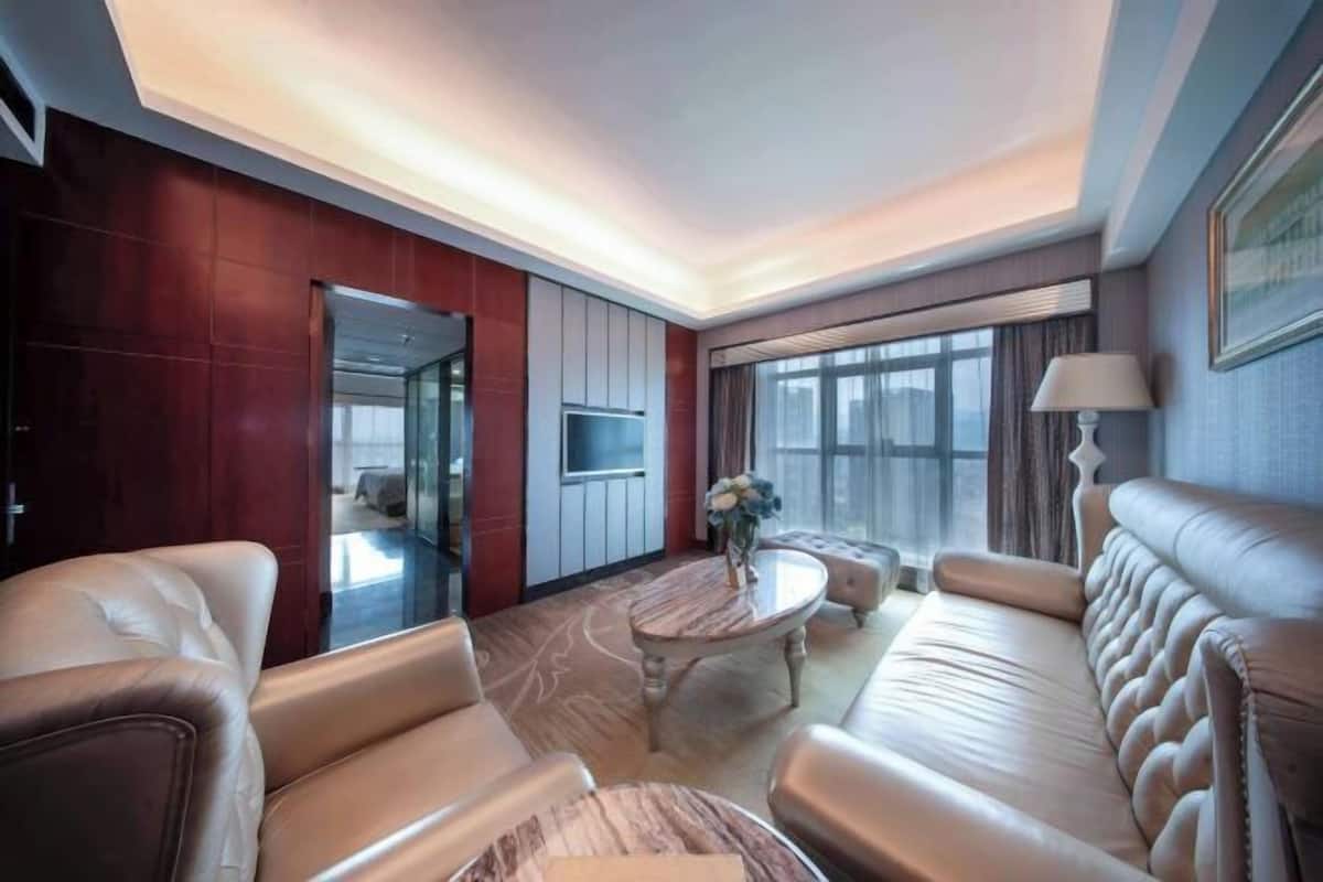 Une chambre d’hôtel moderne avec des canapés en cuir, une table basse en marbre, un téléviseur à écran plat et de grandes fenêtres.