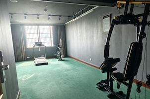 Un gimnasio con equipo de ejercicio, un ventanal grande y una alfombra verde.