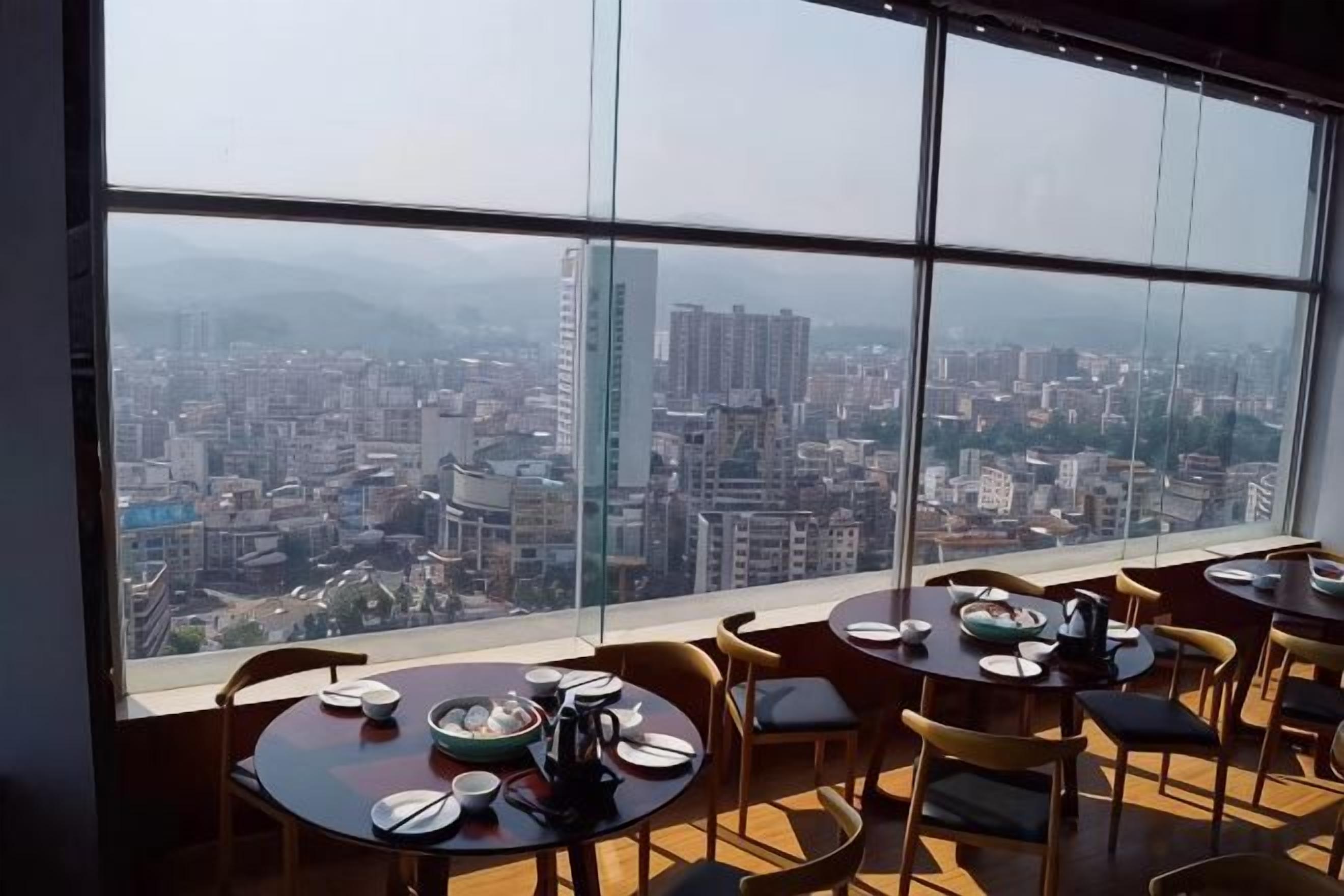 A dining area with tables and chairs, large windows with a city view.