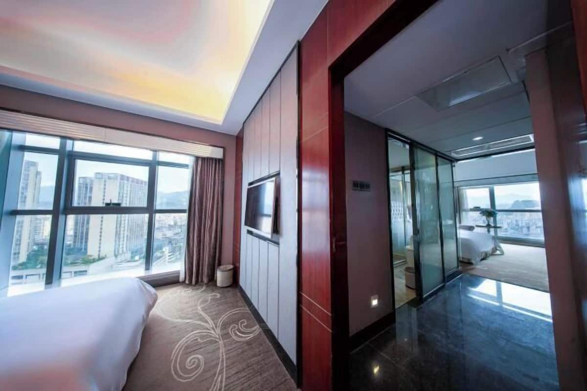 Une chambre d’hôtel avec un grand lit, une télévision et une vue sur la ville grâce à de grandes fenêtres.