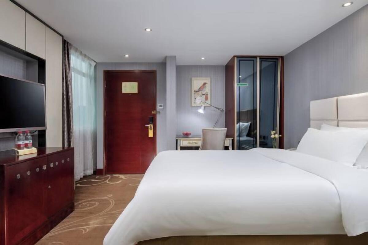 Une chambre d’hôtel avec un grand lit, un bureau avec une chaise, une télévision et une armoire.
