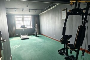 Un gimnasio con equipo de ejercicio, un ventanal grande y una alfombra verde.