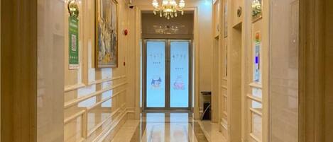 Un pasillo de hotel con un candelabro, obras de arte enmarcadas y un puerta de cristal transparente al final.