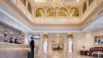 A grand lobby with a reception desk, a chandelier, and classical statues.