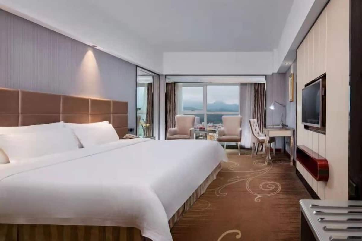 Une chambre d’hôtel avec un grand lit, un bureau, des chaises, une télévision et une vue sur les montagnes.