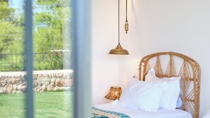 A bedroom with a bed, a hanging lamp, and a wicker headboard. - Sea front! Wonderfull villa with sea views from every room. (Capdepera)