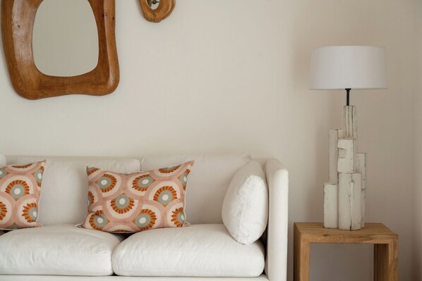 Un canapé blanc agrémenté de coussins à motifs, une petite table en bois avec une lampe, et un élément décoratif en bois fixé au mur.