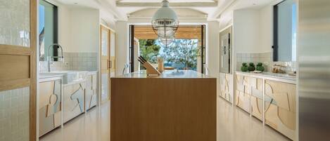 A modern kitchen with a central island, wooden cabinets, and a large window providing a view of the outdoors.
