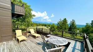 Een houten terras met buitenmeubels, waaronder stoelen en een tafel, met uitzicht op een bergachtig landschap.