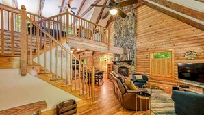 A log cabin interior with a wooden staircase, a fireplace, a television, and a dining area. - Lakefront Log Cabin at Lake Anna, Dock, Deck (Bumpass)