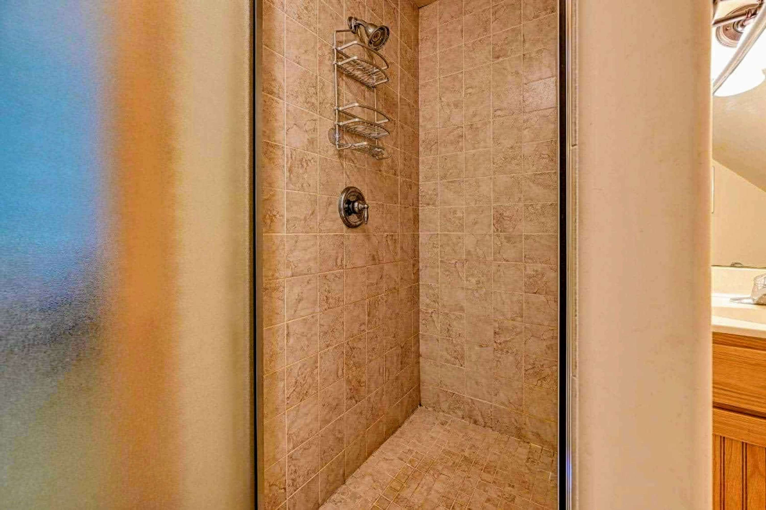A shower with a metal rack and a wall-mounted control.