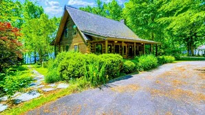 A wooden cabin with a porch, surrounded by lush greenery and a stone pathway. - Lakefront Log Cabin at Lake Anna, Dock, Deck (Bumpass)