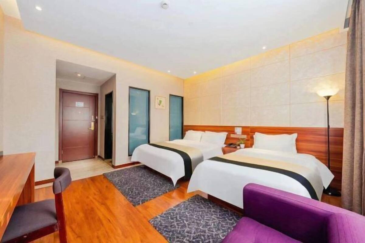 A hotel room with two beds, a desk, a chair, and a lamp.