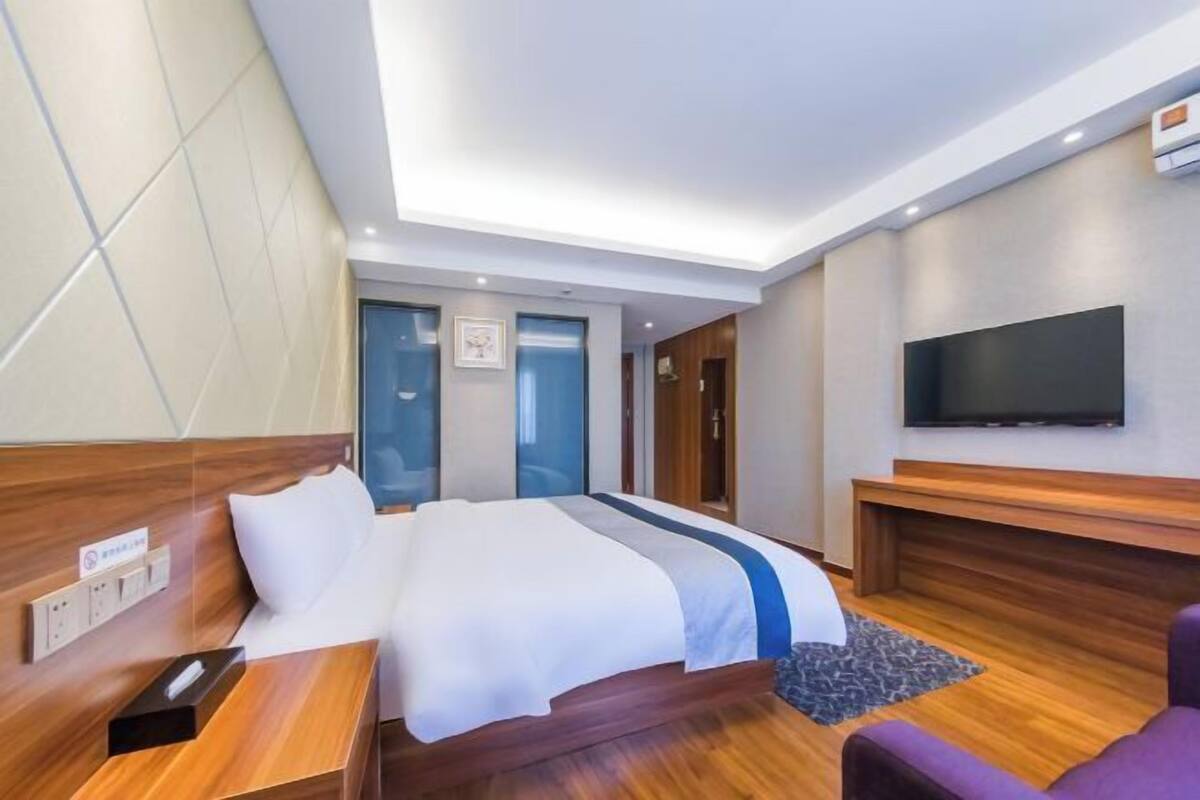 A modern hotel room with a large bed, a flat-screen TV, a wooden headboard, and a small seating area.